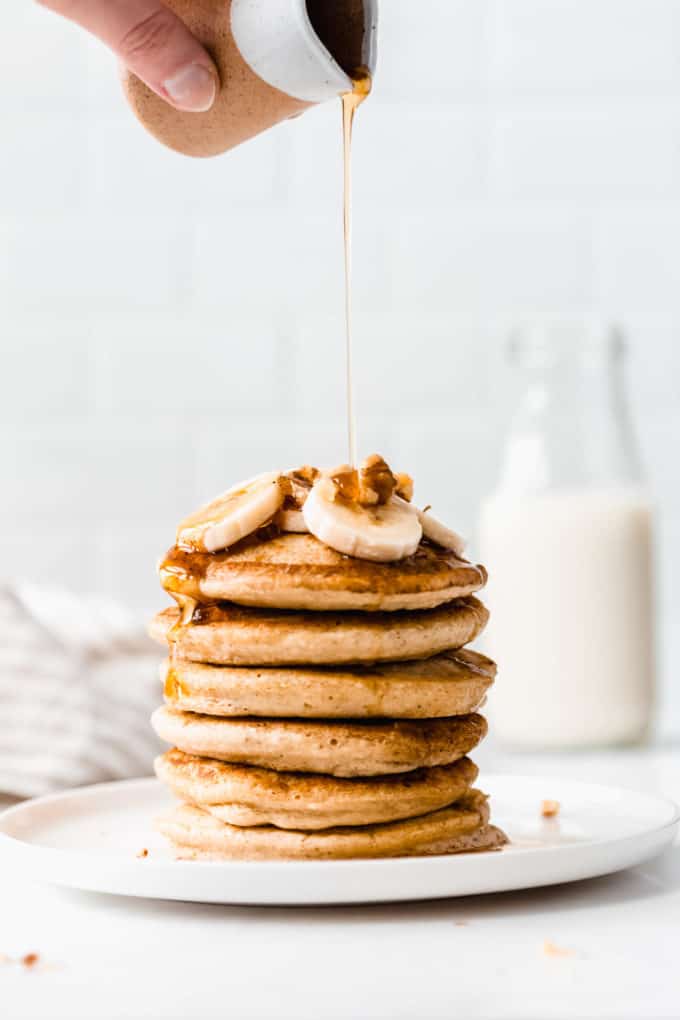 maple syrup being poured onto a stack of oat flour pancakes