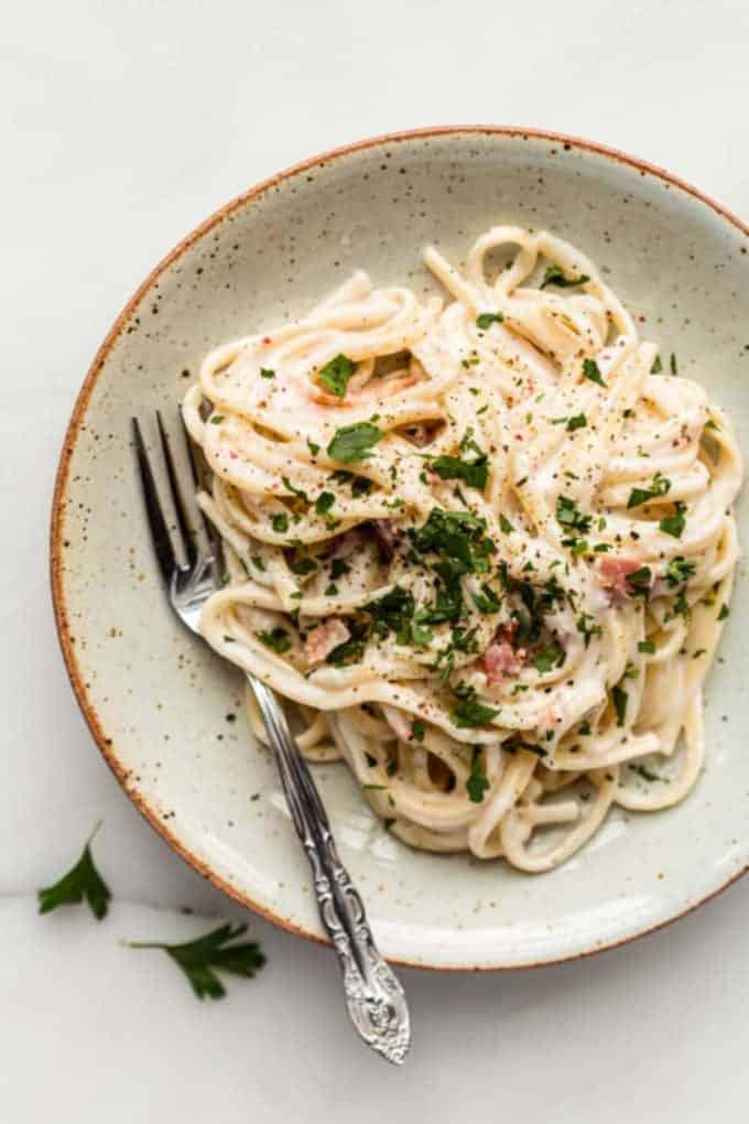 vegan carbonara spaghetti on a white speckled plate with a fork