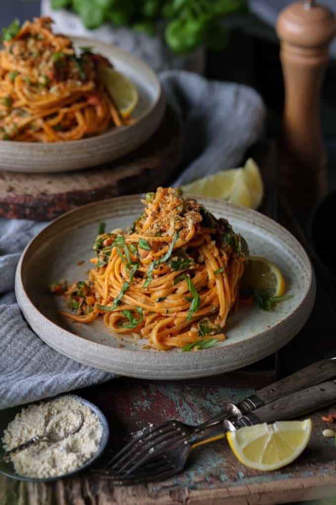 a plate of spaghetti with harissa and lemon wedge on a wood table
