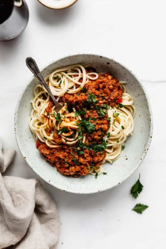 spaghetti topped with lentil bolognese in a white speckled bowl
