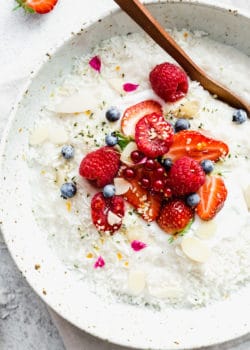 Coconut rice pudding topped with berries, help seeds and shredded coconut in a white speckled bowl