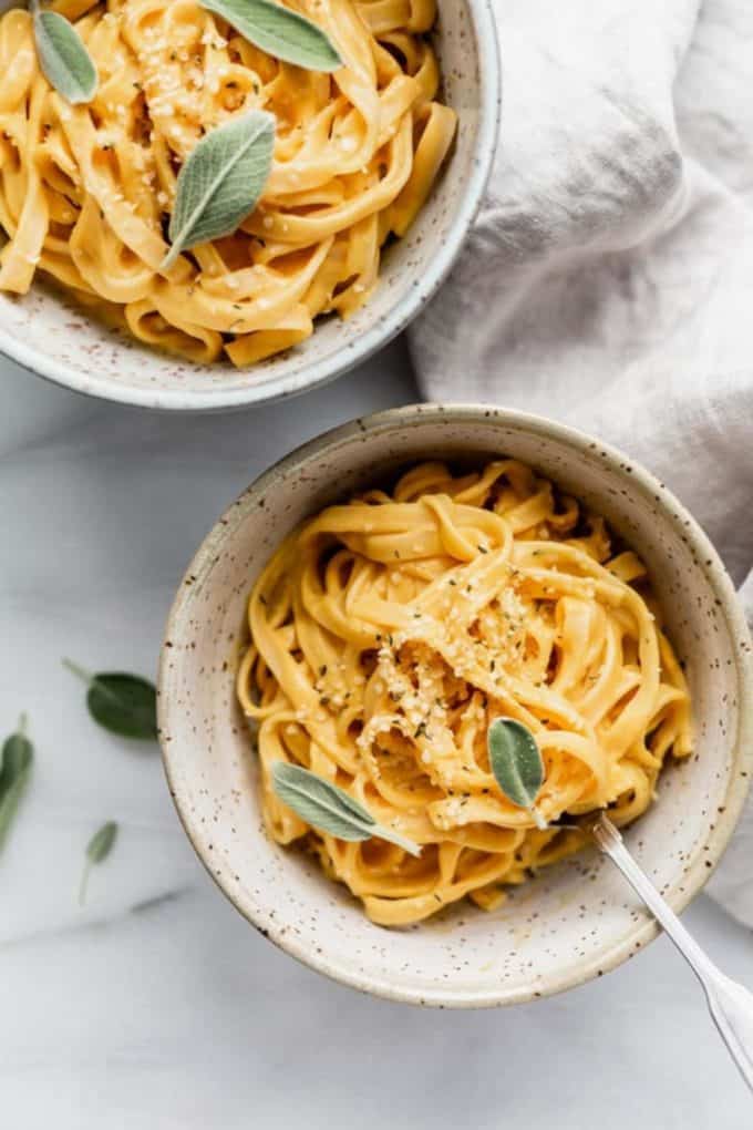 two bowls of linguine with pumpkin Alfredo sauce and sage on them