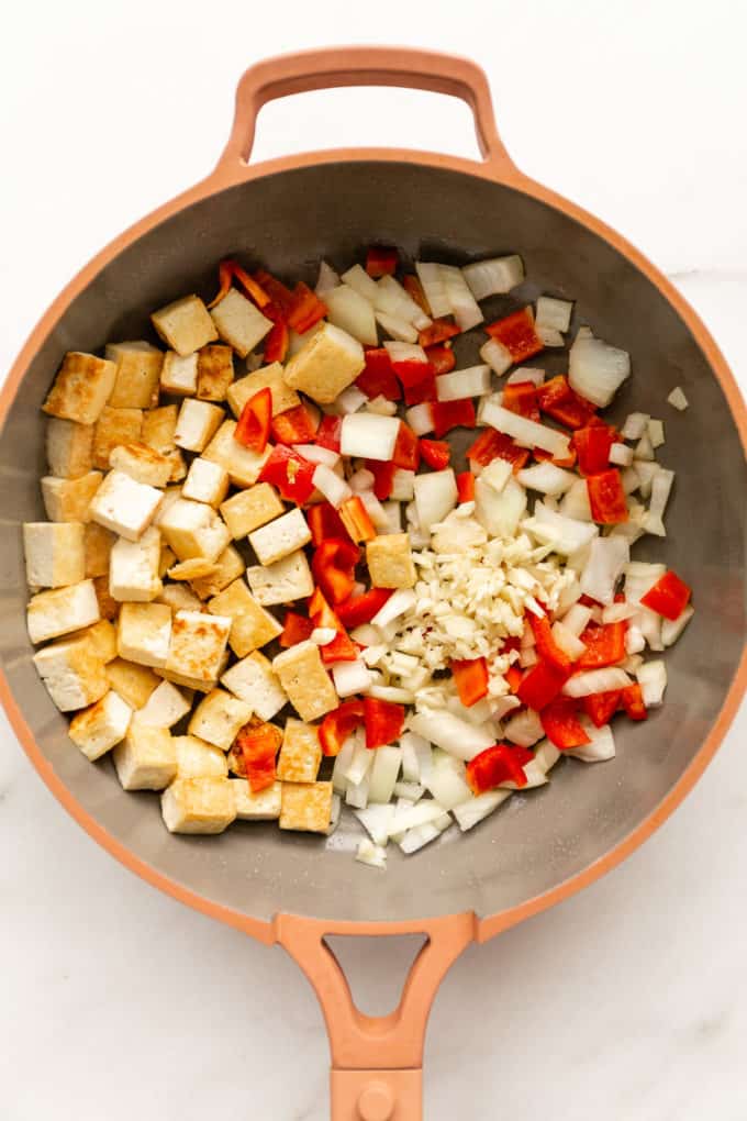 tofu, red peppers, onions and garlic in a pink pan