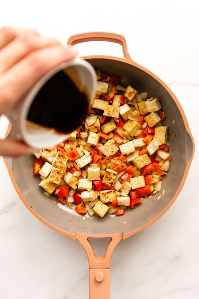 stir-fry sauce being poured into a pan of tofu and vegetables