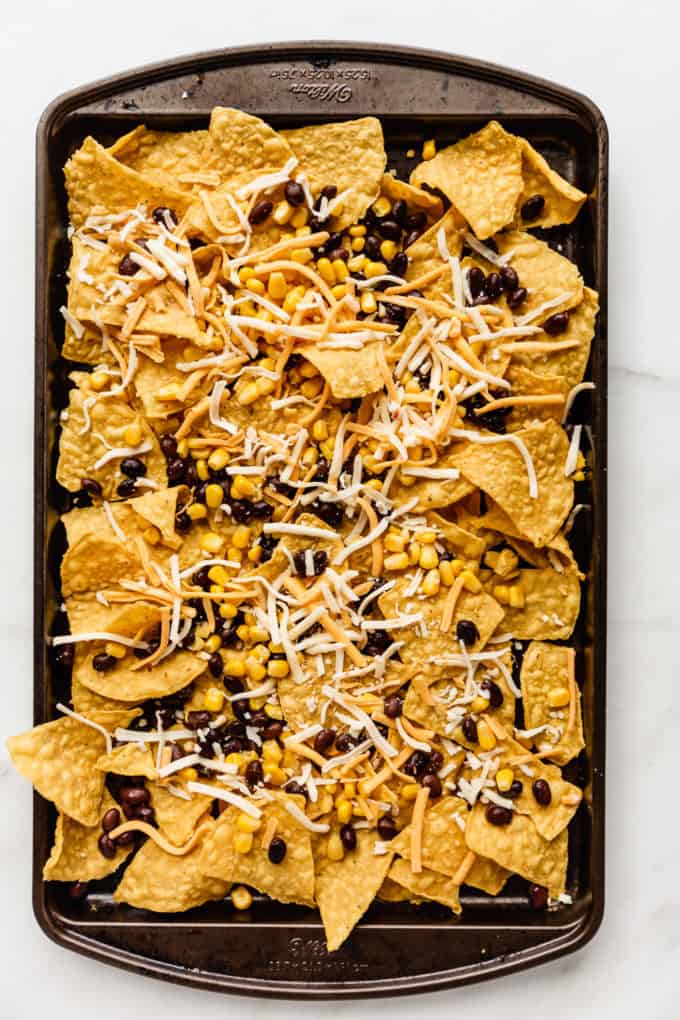 tortilla chips with black beans, corn and cheese on a baking sheet