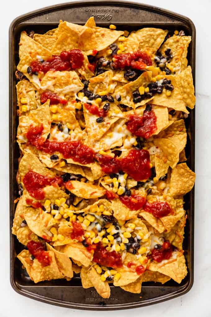 tortilla chips with melted cheese and salsa on a baking sheet