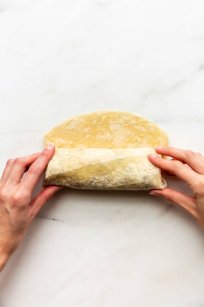 Hands rolling a tortilla into a buritto