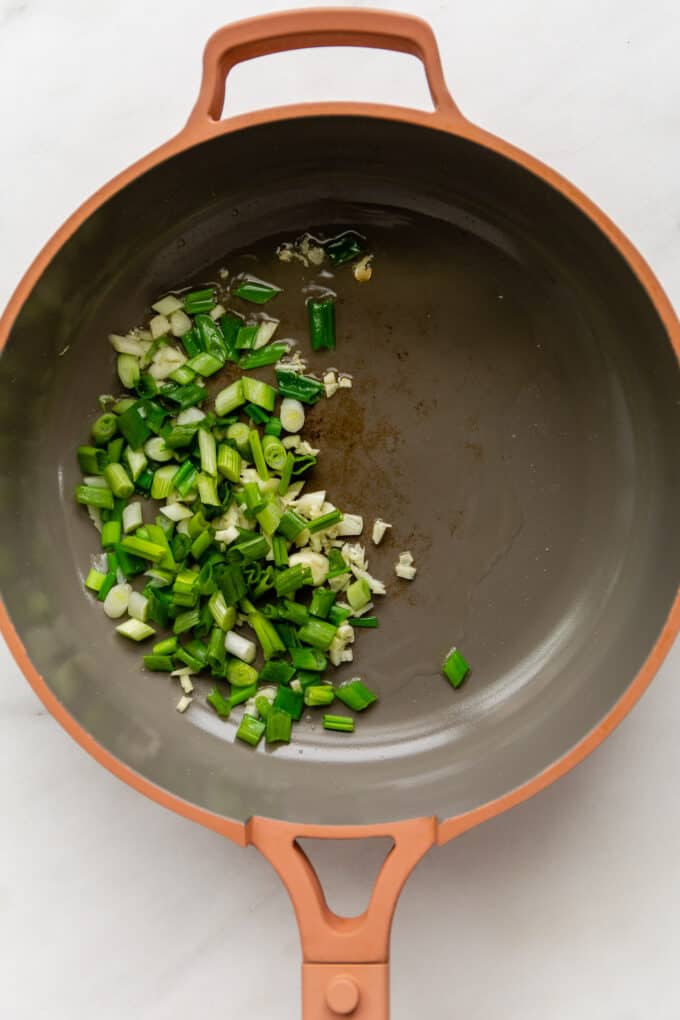 green onions and garlic in a pink pan