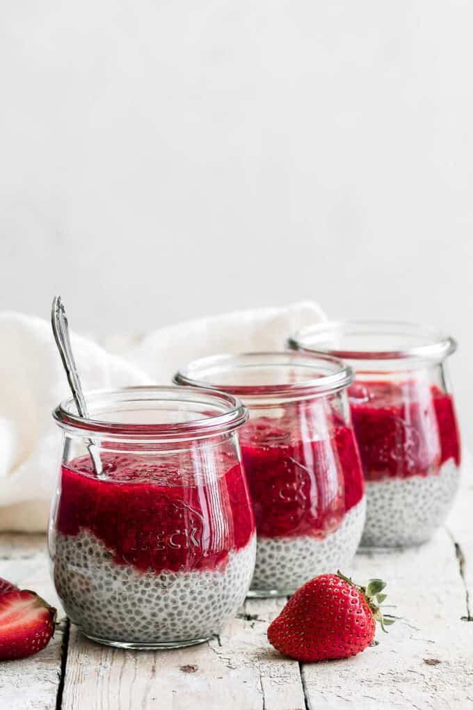three cups of strawberry rhubarb chia pudding with strawberries on the side