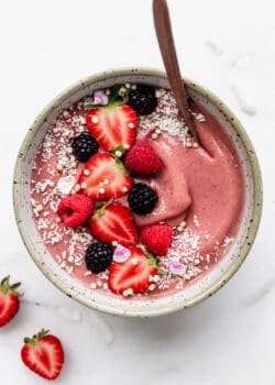a pink smoothie in a white speckled bowl topped with berries