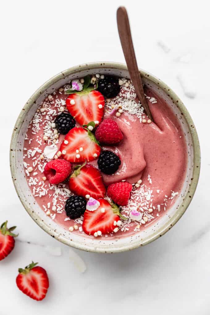 a pink smoothie in a white speckled bowl topped with berries