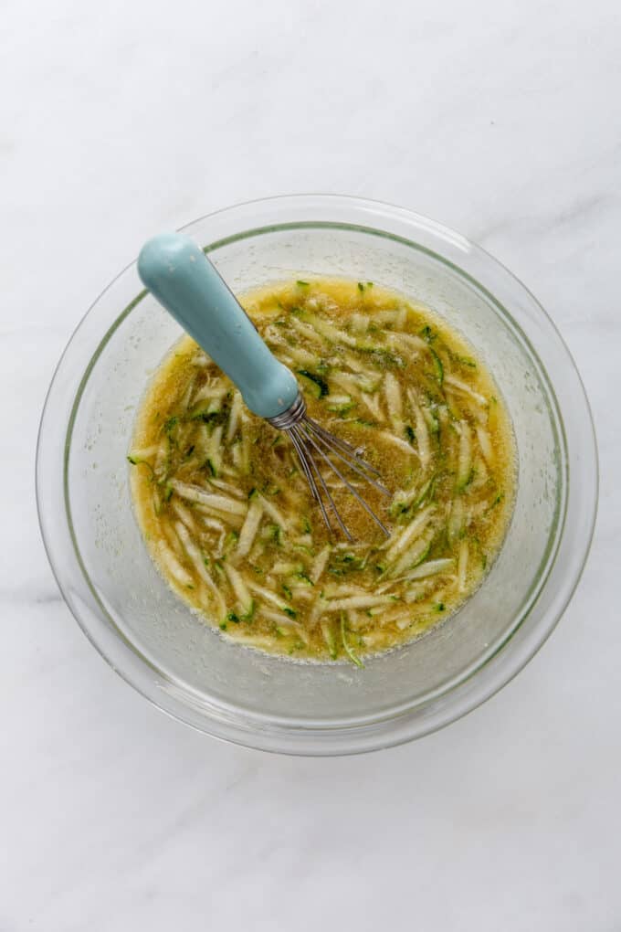 shredded zucchini, eggs and maple syrup in a bowl with a whisk