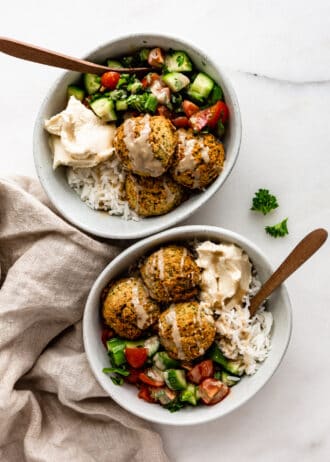 two falafel bowls with wood spoons in them