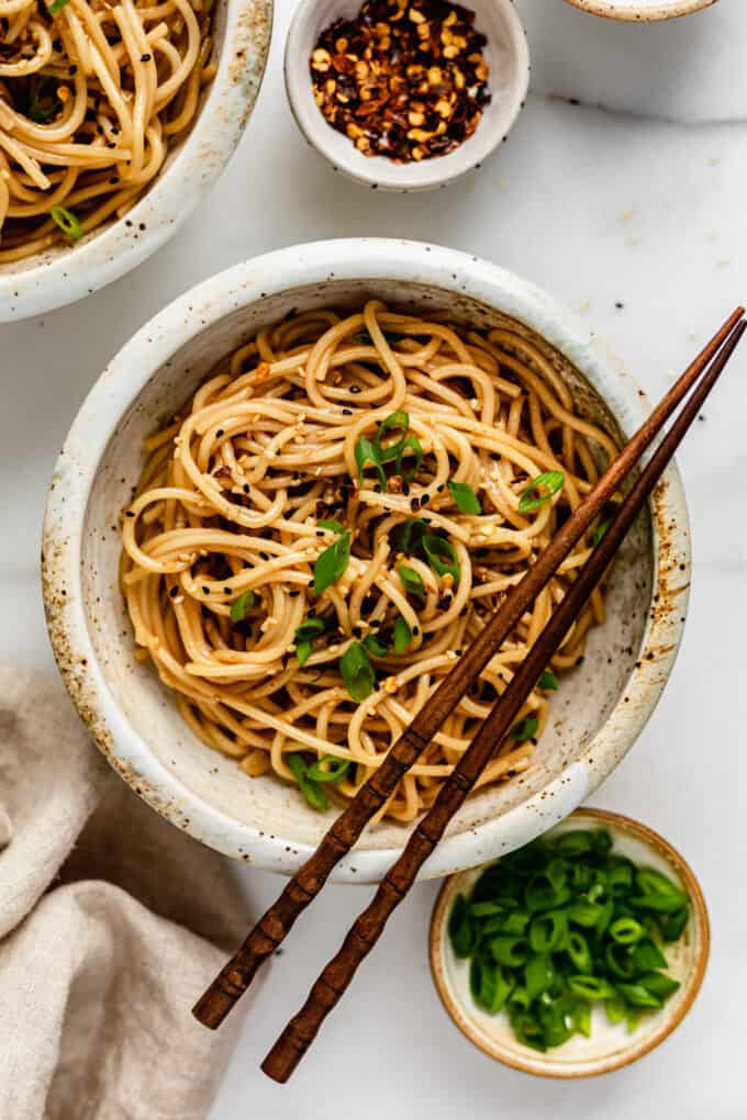 a bowl of garlic noodles with green onions and crushed red peppers in small bowls