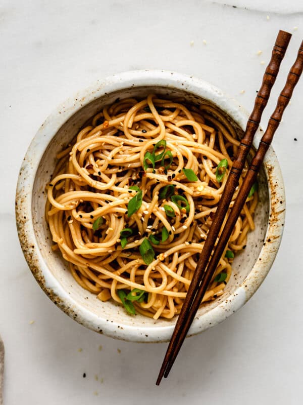 garlic noodles in a white speckled ceramic bowl with wood chopsticks