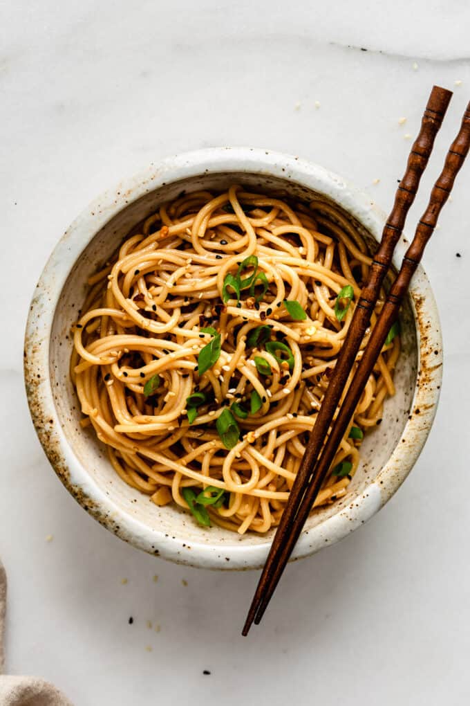 garlic noodles in a white speckled ceramic bowl with wood chopsticks