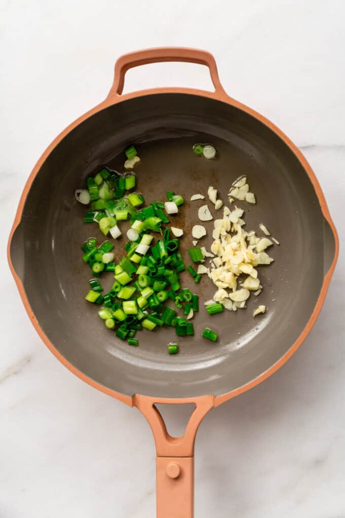 scallions and garlic in a pink pan