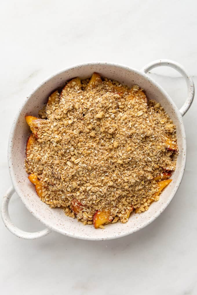 peaches and crisp topping in a white baking dish