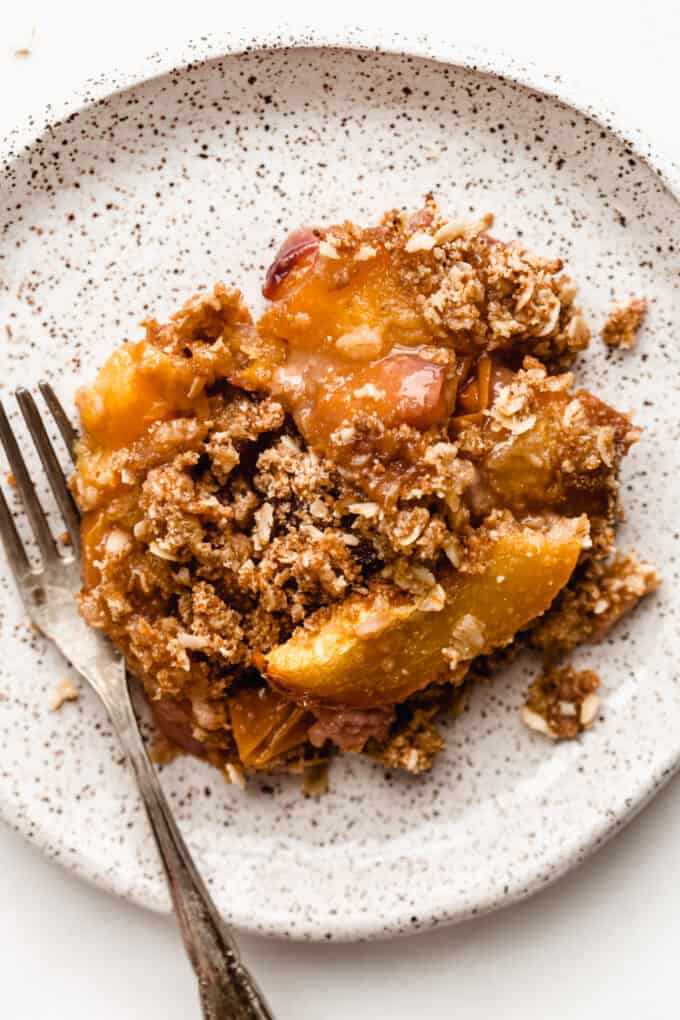 gluten-free peach crisp on a white speckled plate with a fork