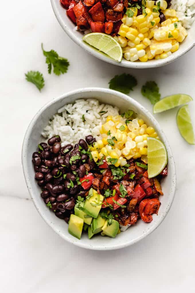 two vegan burrito bowls with vegetables, rice, black beans, peppers and avocado