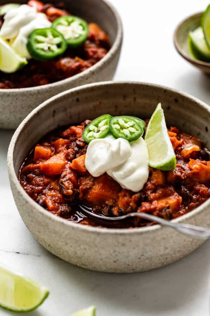 sweet potato chili in a bowl with sour cream, jalapeño peppers and lime