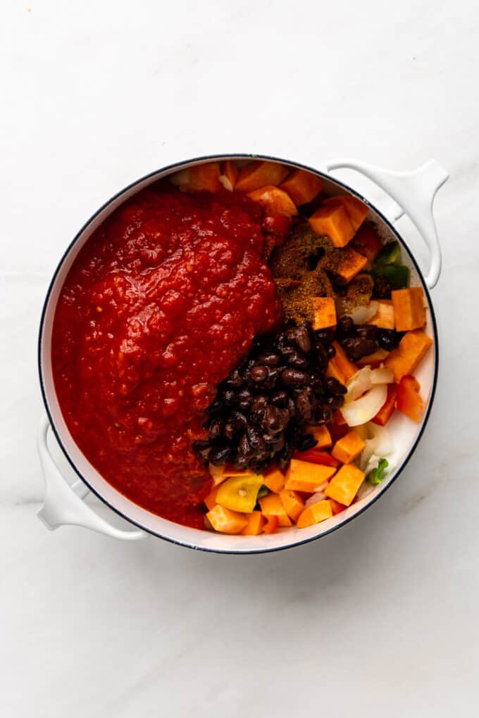 vegetables, sweet potatoes, black beans and crushed tomatoes in a white pot