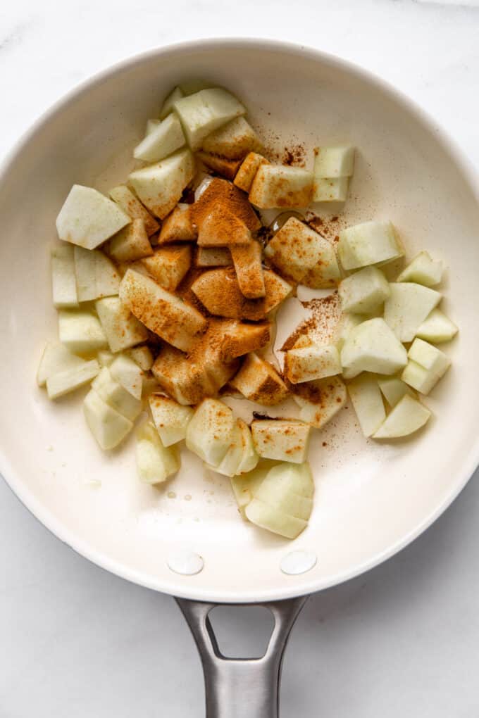 chopped apples with cinnamon and maple syrup in a white pan