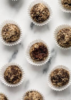 chocolate date balls covered in crushed walnuts on a marble counter