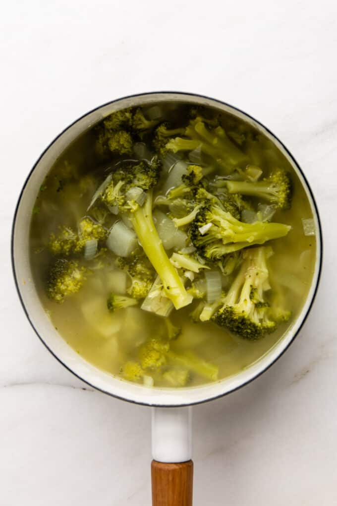 cooked broccoli and potato in broth in a white pot