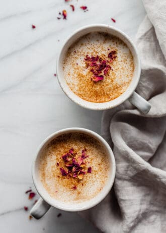 two mugs of chai lattes topped with dried rose petals