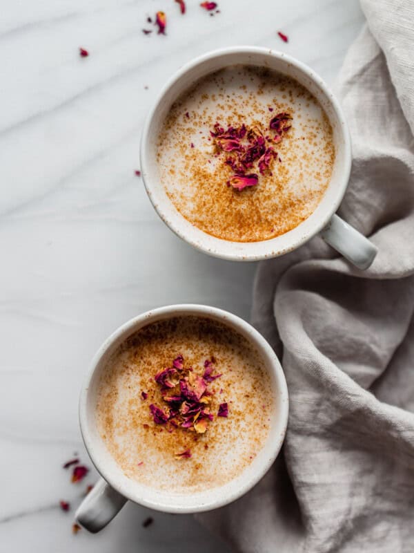 two mugs of chai lattes topped with dried rose petals