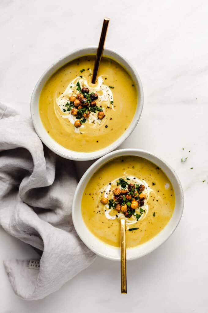 two bowls of curried cauliflower soup with gold spoons in them