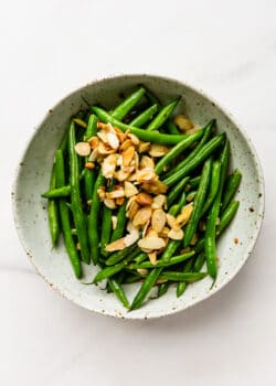 Green beans in a white speckled bowl topped with sliced almonds