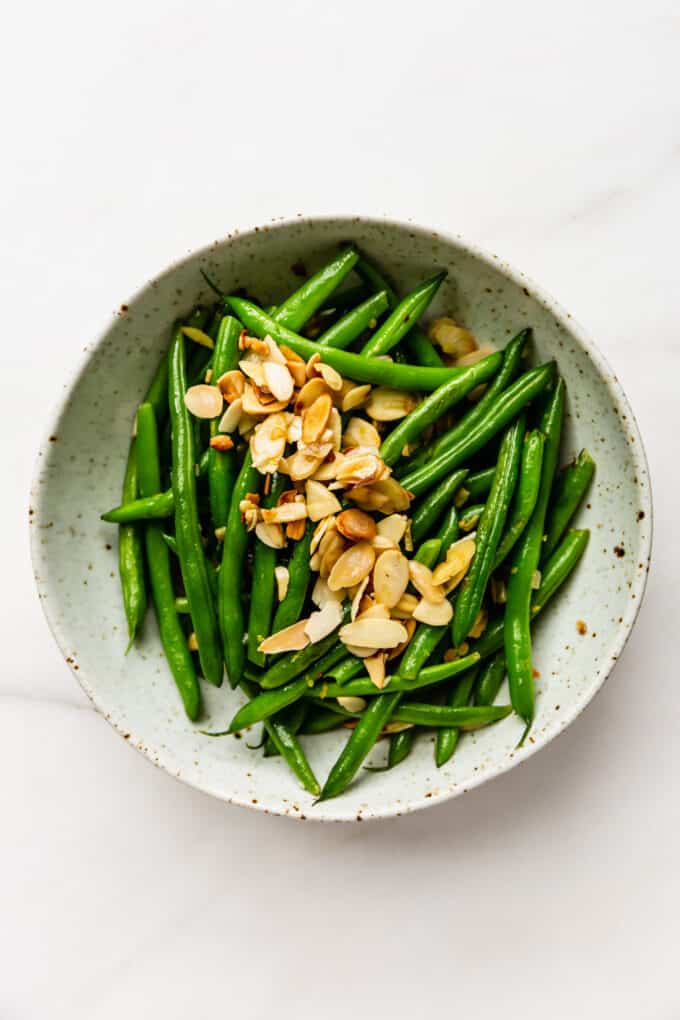 Green beans in a white speckled bowl topped with sliced almonds