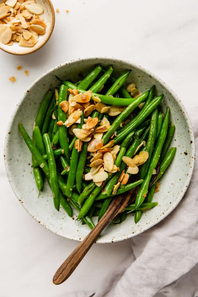 a bowl of green beans almondine with a wood serving spoon