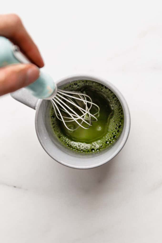 a whisk whisking matcha and water in a mug