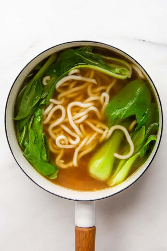 udon noodle soup with bok choy in a white pot