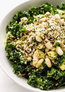 close up of kale salad in a bowl with white beans, avocado and seeds