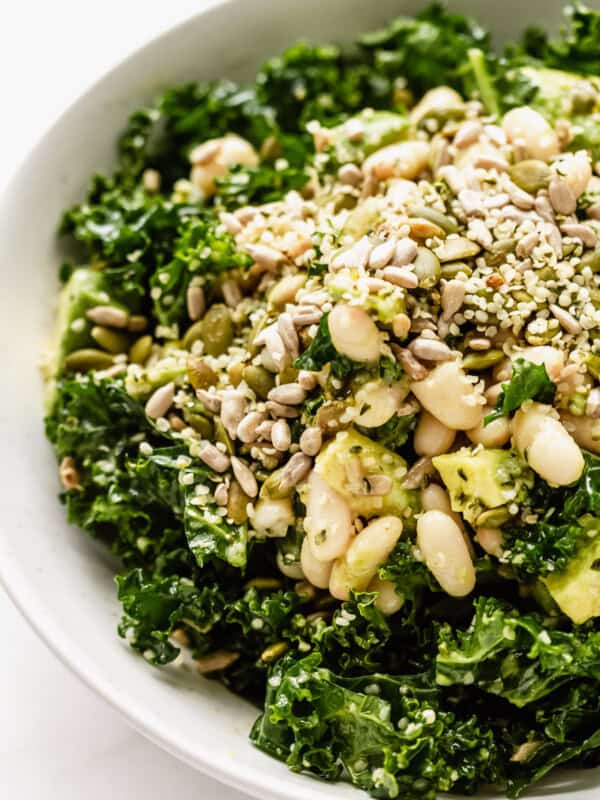 close up of kale salad in a bowl with white beans, avocado and seeds
