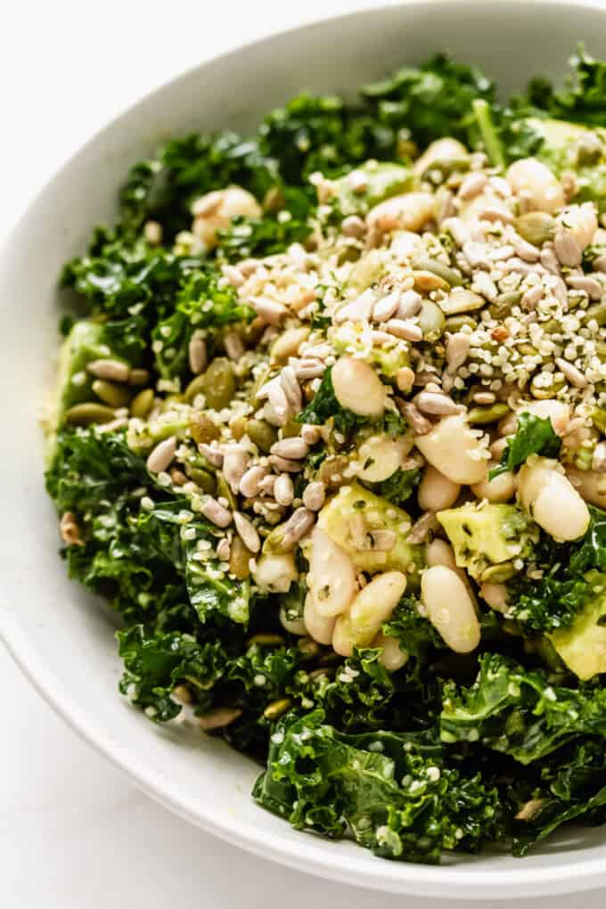 close up of kale salad in a bowl with white beans, avocado and seeds