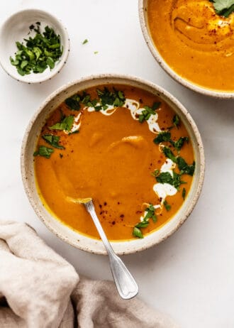 two bowls of sweet potato carrot and ginger soup with a napkin on the side