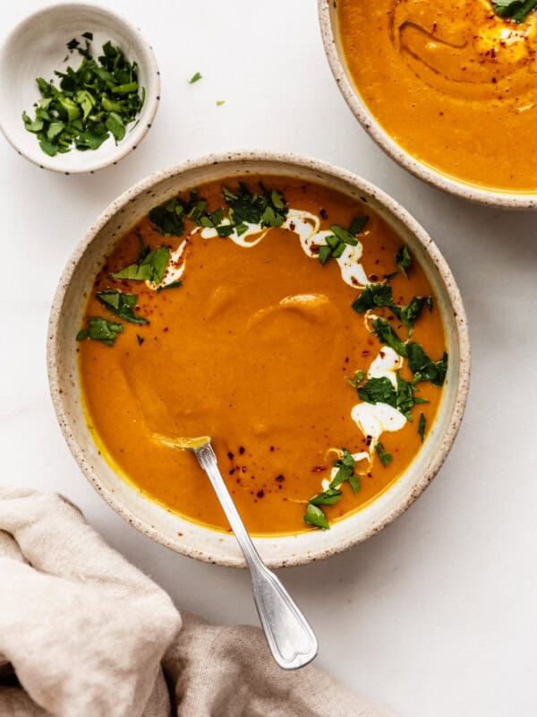two bowls of sweet potato carrot and ginger soup with a napkin on the side