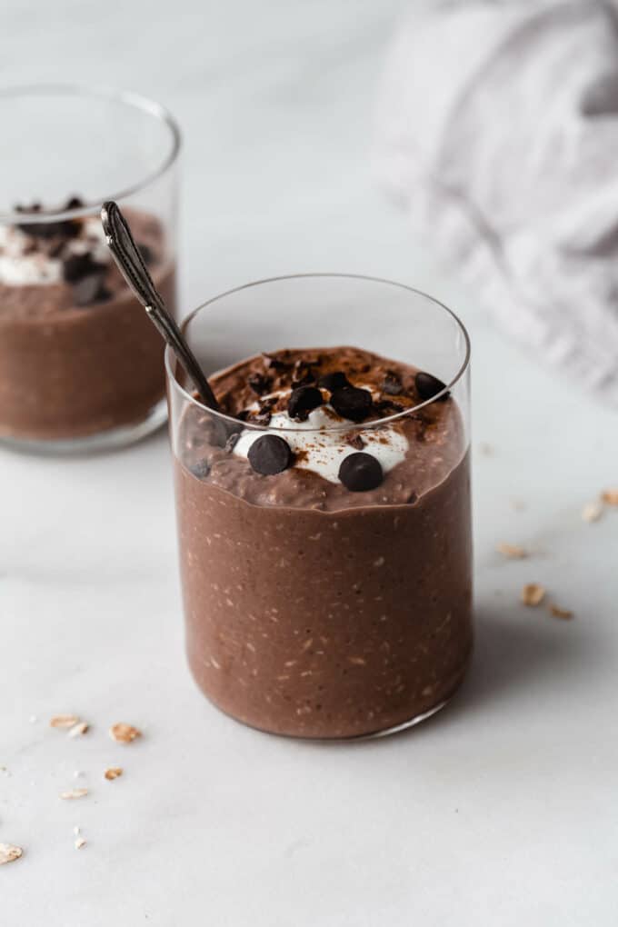 two cups of chocolate overnight oats topped with yogurt and chocolate chips