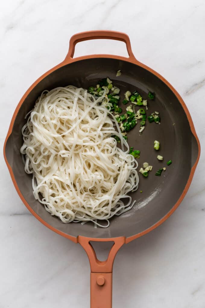 rice noodles with scallions and garlic in a pink pan