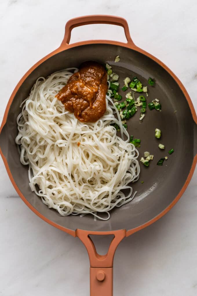rice noodles, sesame sauce and scallions in a pink pan