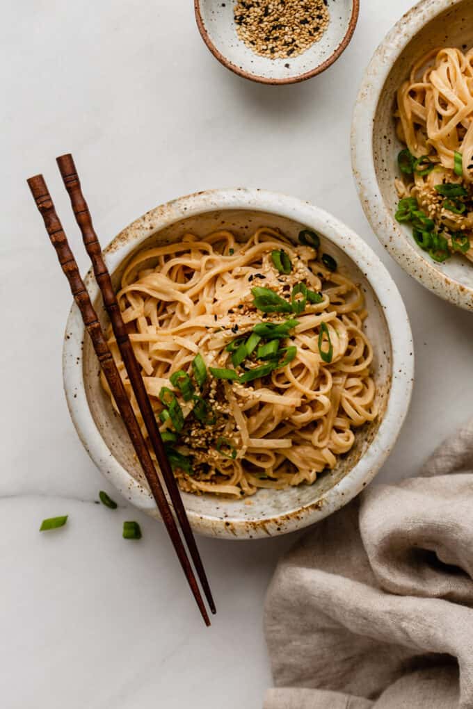 two bowls of sesame noodles topped with scallions and sesame seeds