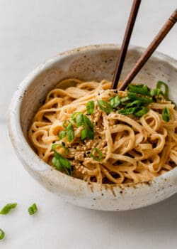sesame noodles in a ceramic speckled bowl topped with scallions and sesame seeds