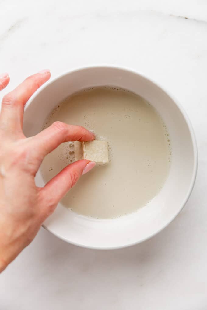 a piece of tofu being dipped into a bowl of almond milk