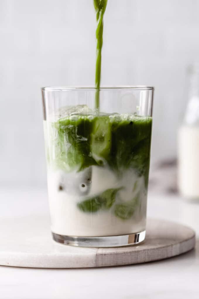 matcha being poured into a glass of oat milk