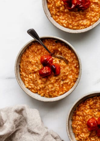 three bowls of tomato risotto topped with roasted tomatoes and basil